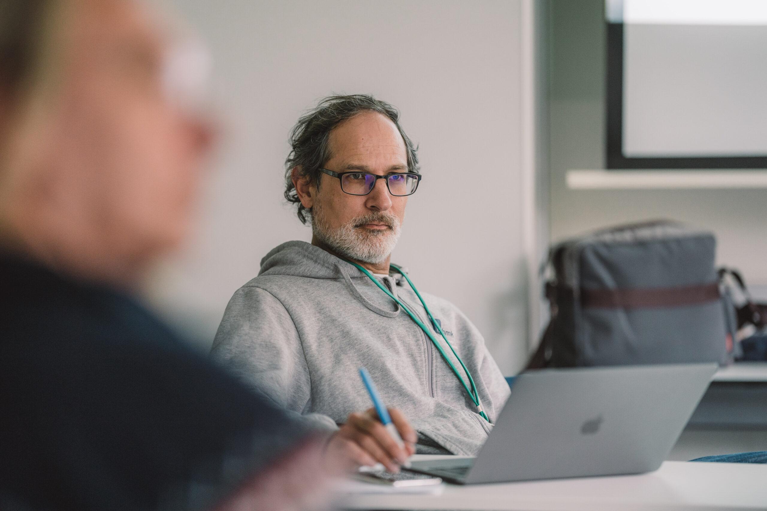 Ein Mann in grauem Pullover sitzt an einem Laptop und hört einem Gespräch zu. Bild: D64/Fionn Große