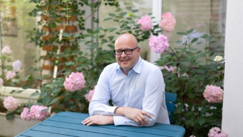 Leonhard Dobusch sitz vor rosa Hortensien an einem Türkisblauen Tisch. Bild: CC-BY 4.0 Jana Madzigon