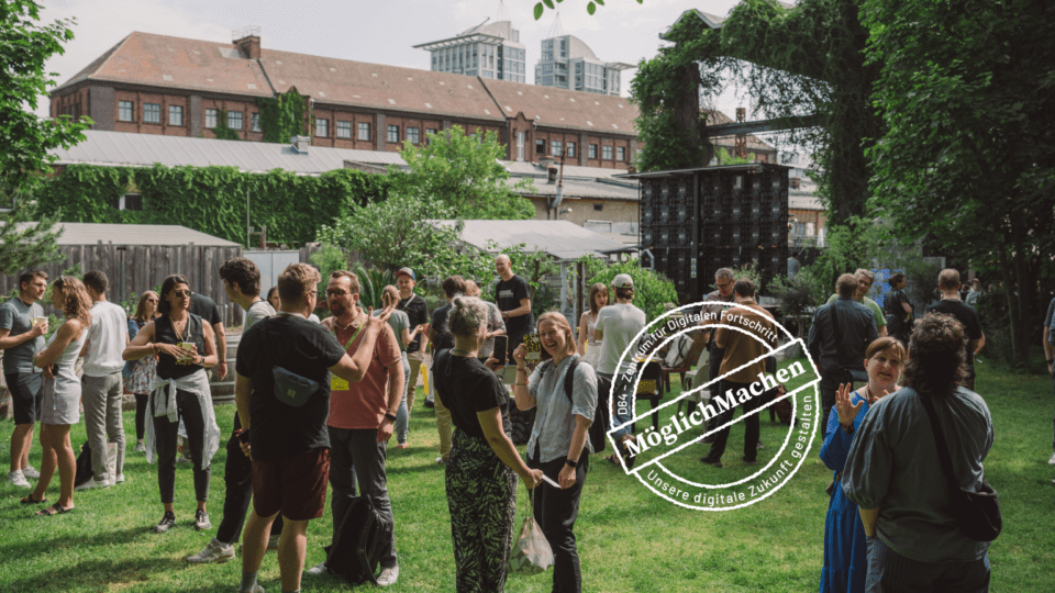 D64-Mitglieder stehen auf einer grünen Wiese vor einer Veranstaltungshalle und diskutieren. Bild: D64/Fionn Große