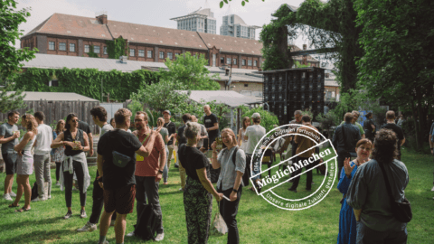 D64-Mitglieder stehen auf einer grünen Wiese vor einer Veranstaltungshalle und diskutieren. Bild: D64/Fionn Große