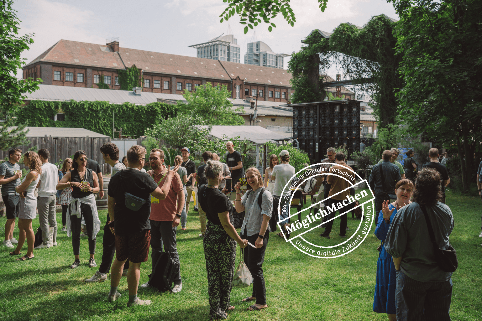 D64-Mitglieder stehen auf einer grünen Wiese vor einer Veranstaltungshalle und diskutieren. Bild: D64/Fionn Große